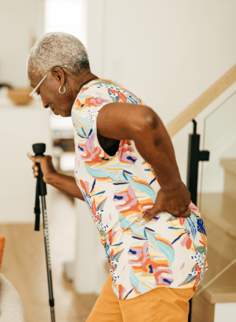 The image shows a older black woman with a walking stick with her hand holding her hip. 